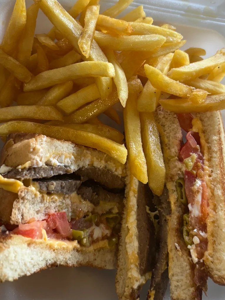 A hot sandwich cut into halves on toasted bread — sliced meat, melted cheese, tomato and sliced peppers — with a large portion of french fries